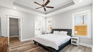 A bedroom with a bed, a ceiling fan, a dresser, a vanity, and a window with blinds.