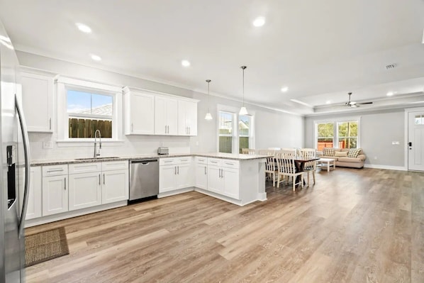 A spacious kitchen with white cabinets, a dishwasher, and a dining area with a table and chairs. - Perfect Beach Getaway Near 30A, Sunnyside & PCB! (Panama City Beach)