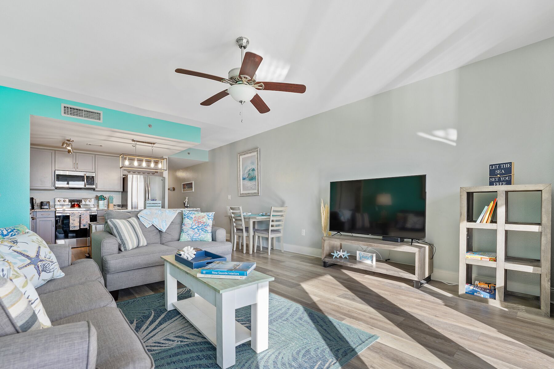 A modern living room with a sofa, coffee table, TV, and a kitchen area in the background.