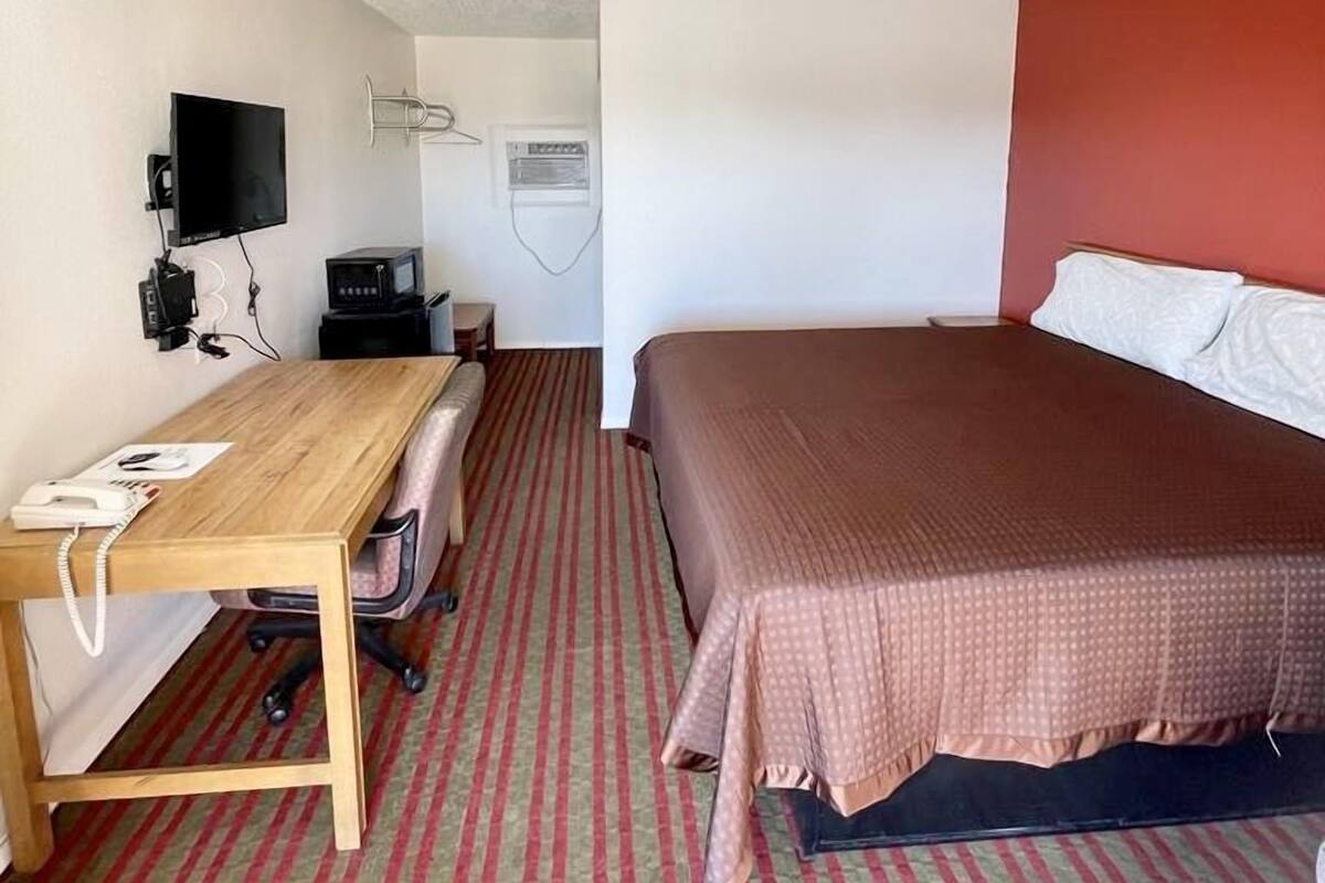 A hotel room with a bed, a desk with a telephone, a television, and a small table.