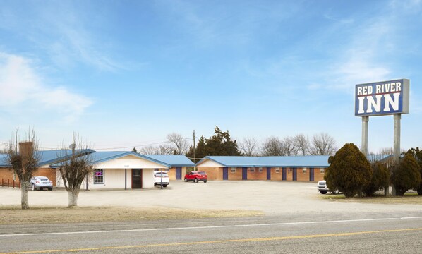 Un hôtel appelé Red River Inn, avec une grande enseigne, un parking et un bâtiment doté d’un toit bleu.