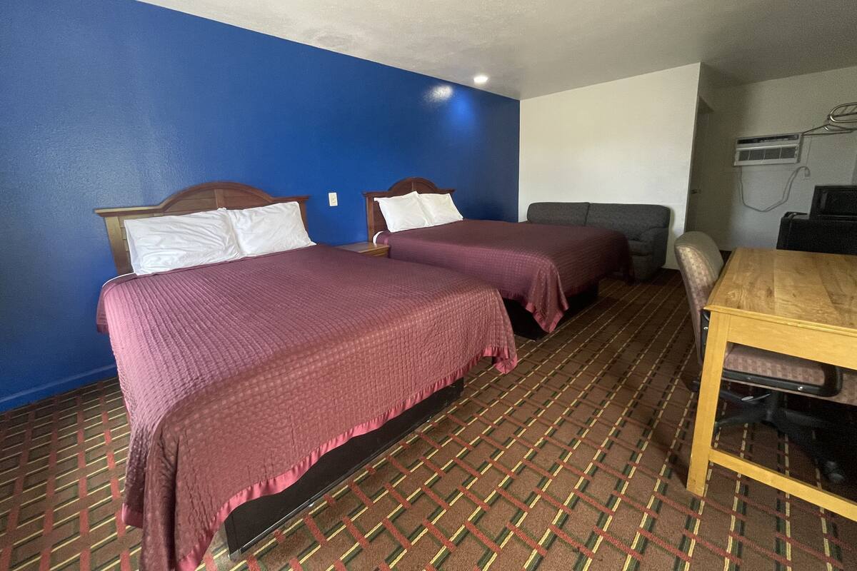 A hotel room with two beds, a sofa, a table, and an air conditioning unit.