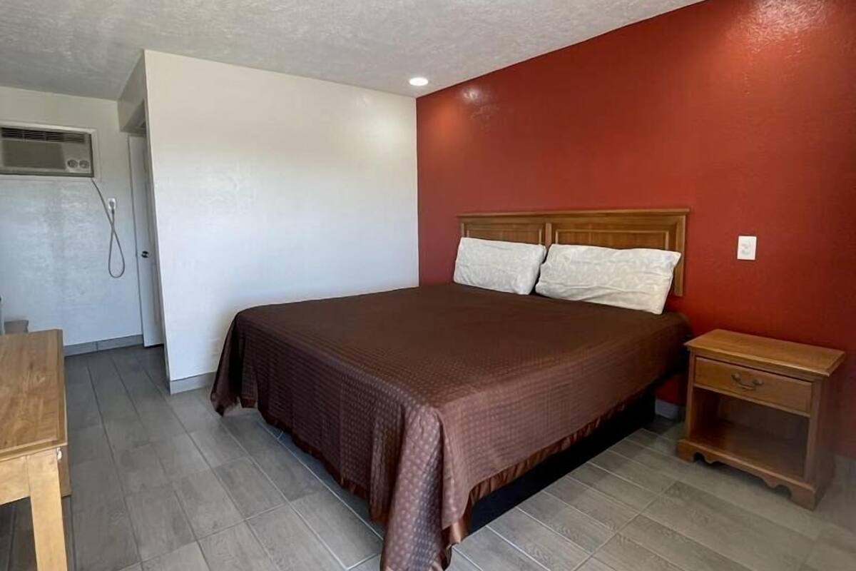 A single bedroom with a bed, a nightstand, a wooden table, and a wall-mounted air conditioning unit.
