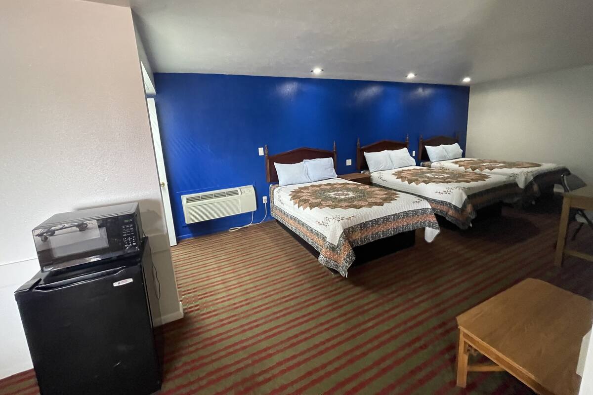 A hotel room with two beds, a refrigerator, a heater, and a small wooden table.