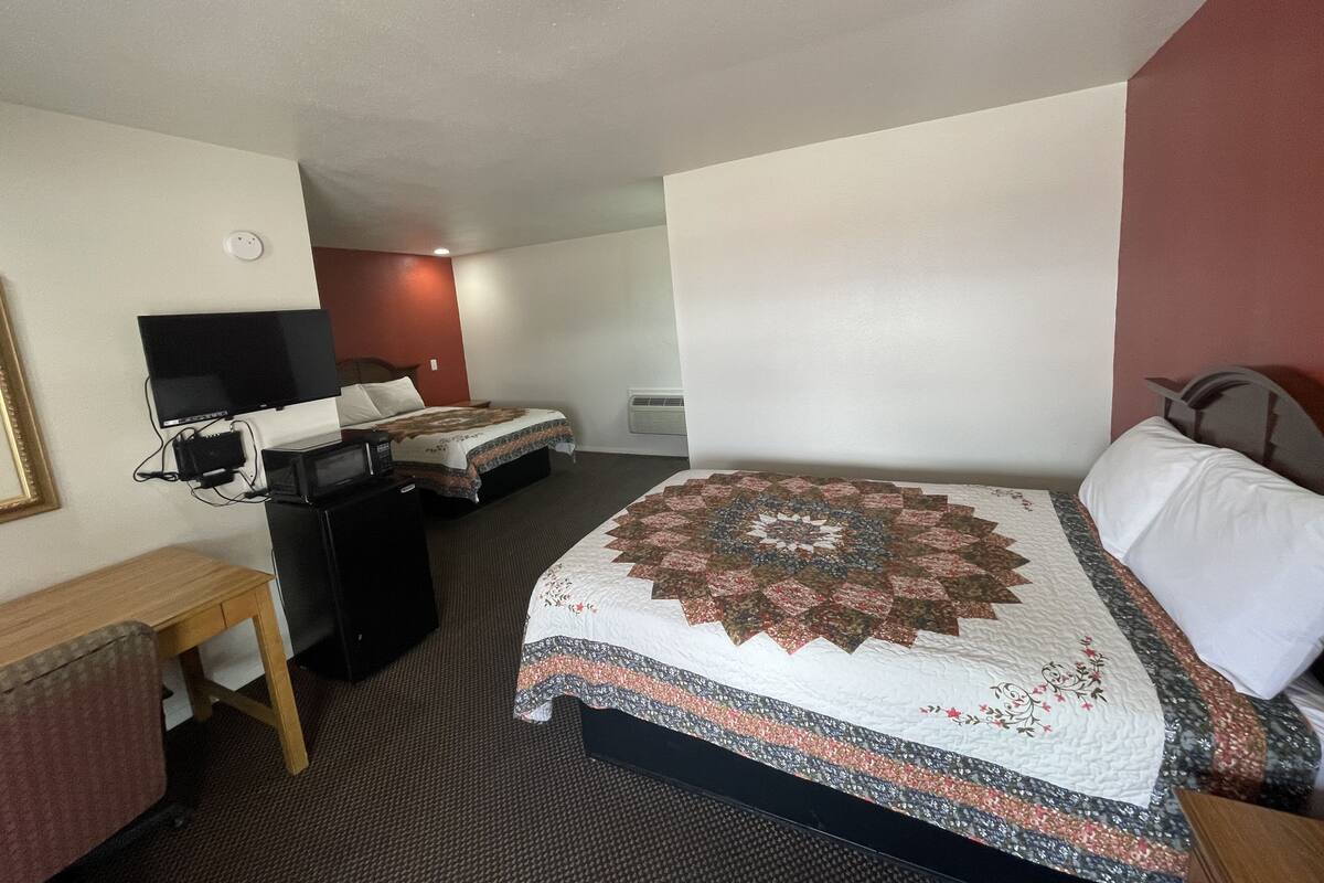 A hotel room with a bed, a desk, a television, and a wall-mounted air conditioning unit.