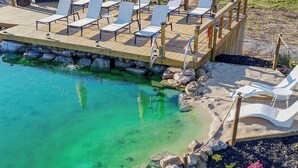 Ein Poolbereich mit Liegestühlen und Sonnenschirmen, umgeben von einem Holzboden und einer Steinumrandung.