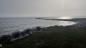 A coastal landscape with a grassy area, rocks, and a calm sea under a bright sun. - Book Now for Fun  in the Sun! Spring  & Summer 2026  (Narragansett)