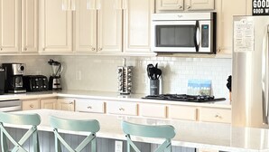 A kitchen with white cabinets, a stainless steel refrigerator, a microwave, a stove, and bar stools. - Book Now for Fun  in the Sun! Spring  & Summer 2026  (Narragansett)