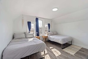 A bedroom with two beds, a window with curtains, a bedside table, and a rug.