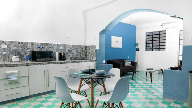 A modern kitchen with a checkered floor, white cabinets, and a dining area with chairs and a table. - Casa 66 (Mérida)