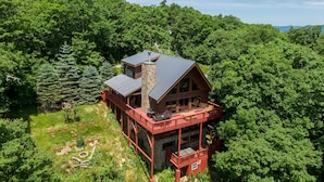 A log cabin with a stone chimney, multiple decks, and surrounded by dense forest. - Carolina Lookout - 10 mins to downtown Boone, hot tub, ping pong, long mountain views (Boone)