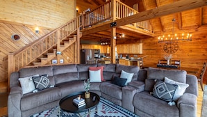 A wooden interior with a large sectional sofa, a staircase, and a kitchen area. - Carolina Lookout - 10 mins to downtown Boone, hot tub, ping pong, long mountain views (Boone)