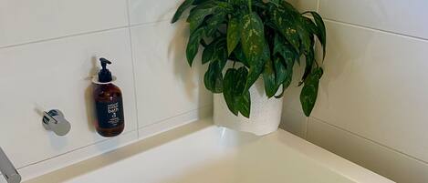A bathroom with a white bathtub, a green plant, and a bottle of bubble bath.