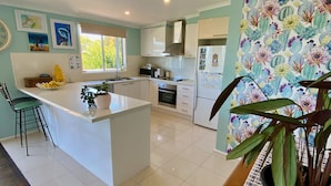 A modern kitchen with a central island, white cabinetry, and a large window providing natural light. - Salty Paws Dog Friendly Luxe Cottage (San Remo)