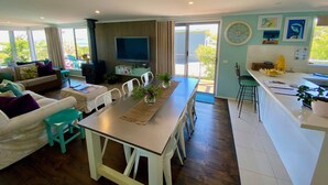 A modern living room with a sofa, dining table, and kitchen area. - Salty Paws Dog Friendly Luxe Cottage (San Remo)