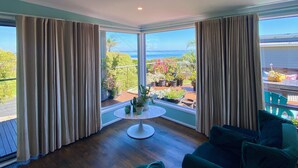 A room with a view of the sea, a round table with a plant, and two green sofas. - Salty Paws Dog Friendly Luxe Cottage (San Remo)