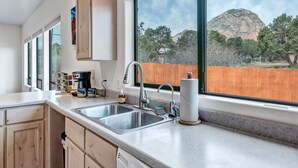 Una cocina con dos fregaderos, una cafetera y un ventanal con vistas a una montaña y árboles.