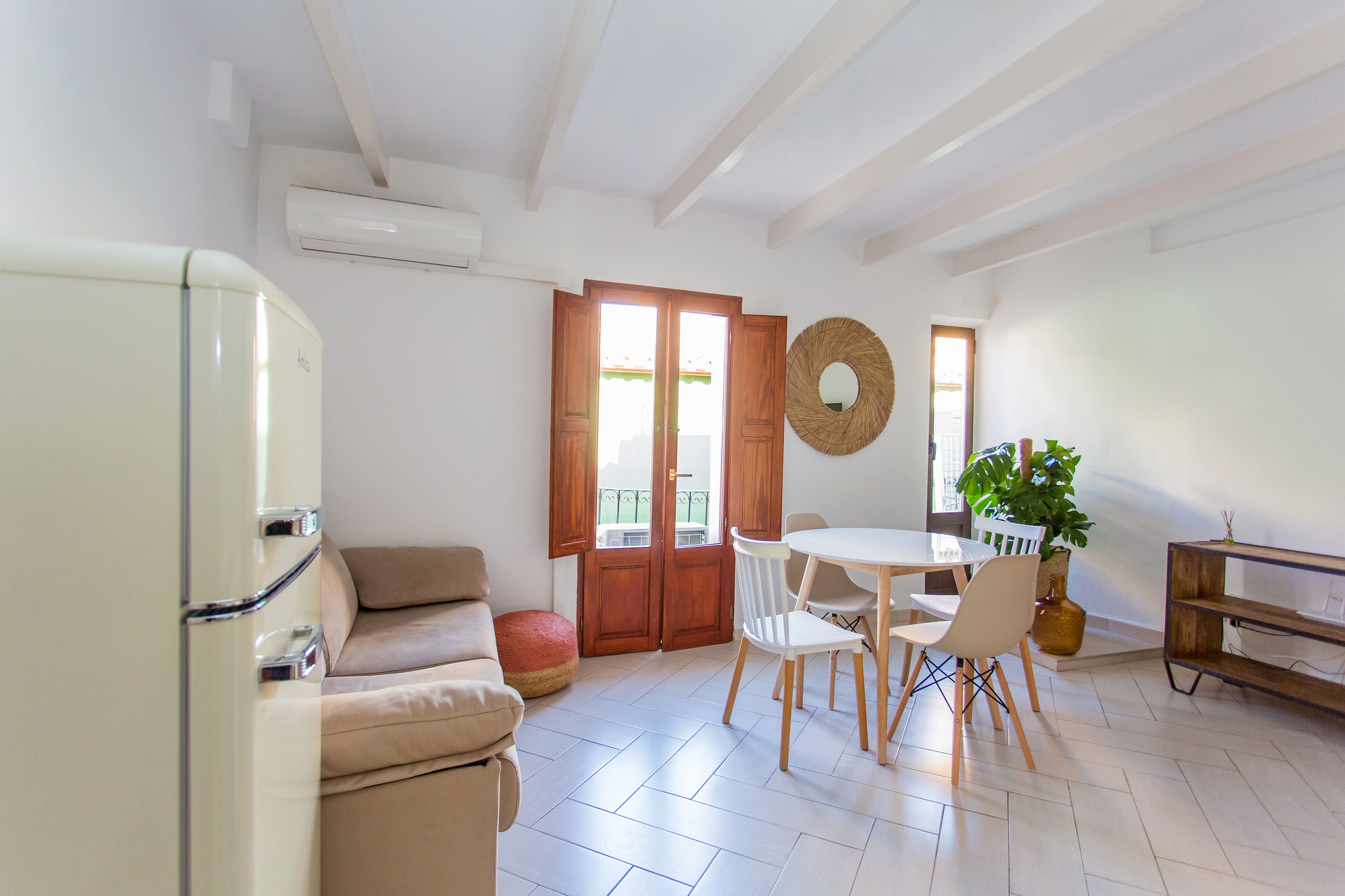 A modern kitchen with a white refrigerator, a beige sofa, and a dining area with a round table and chairs.