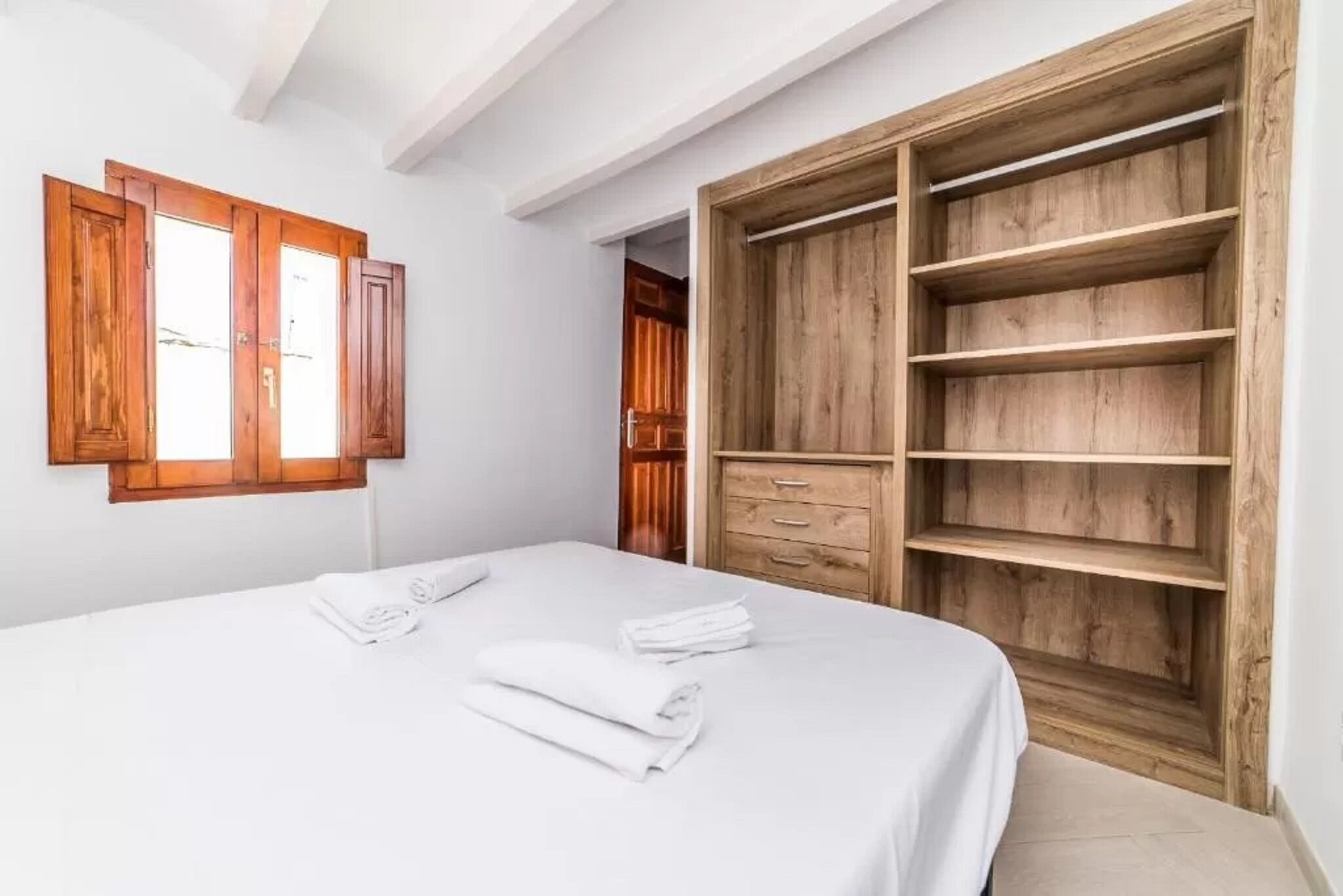 Un dormitorio con cama, armario de madera y ventana con contraventanas de madera.