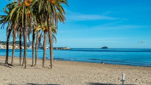 A beach with palm trees, a wooden deck, and a clear blue sky. - Alojamientos la Vila Mayor 7 (Villajoyosa)