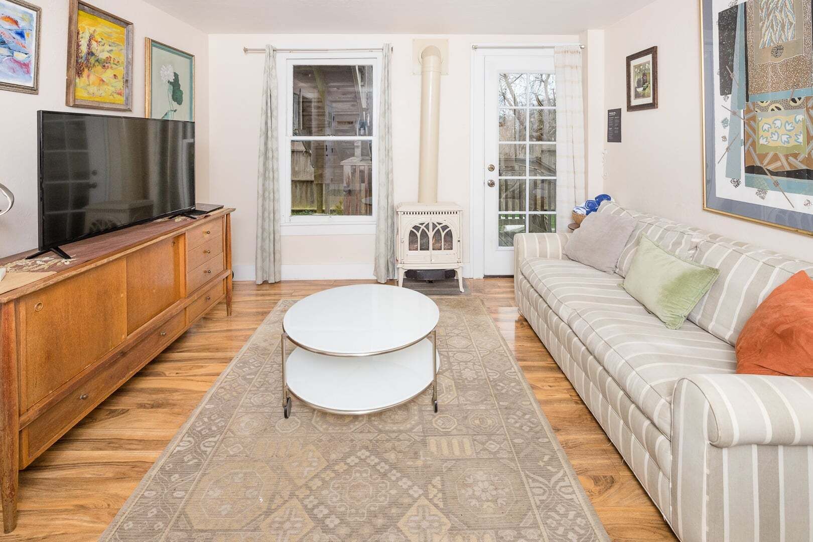 A living room with a TV, wooden cabinet, white sofa, and patterned rug.