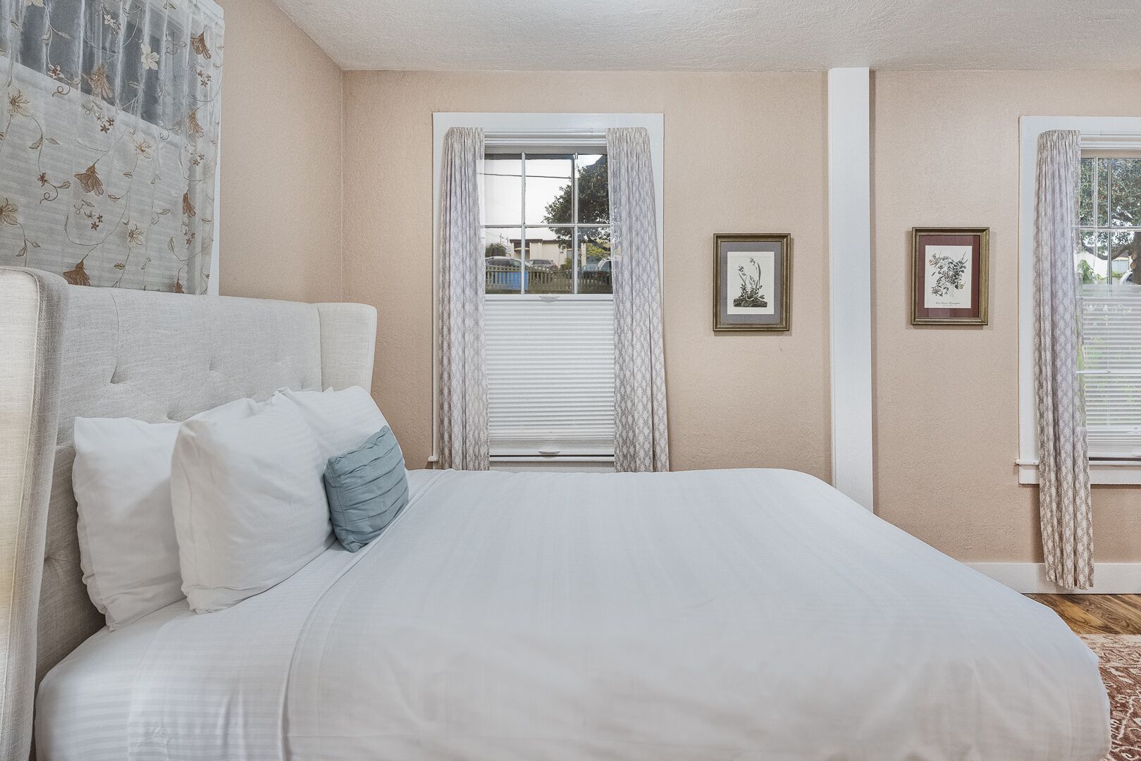 A bedroom with a large bed, a headboard, and two windows with curtains.