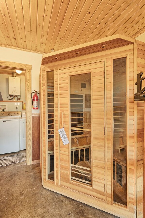 A sauna with wooden walls and a glass door, a fire extinguisher, and a visible water heater.