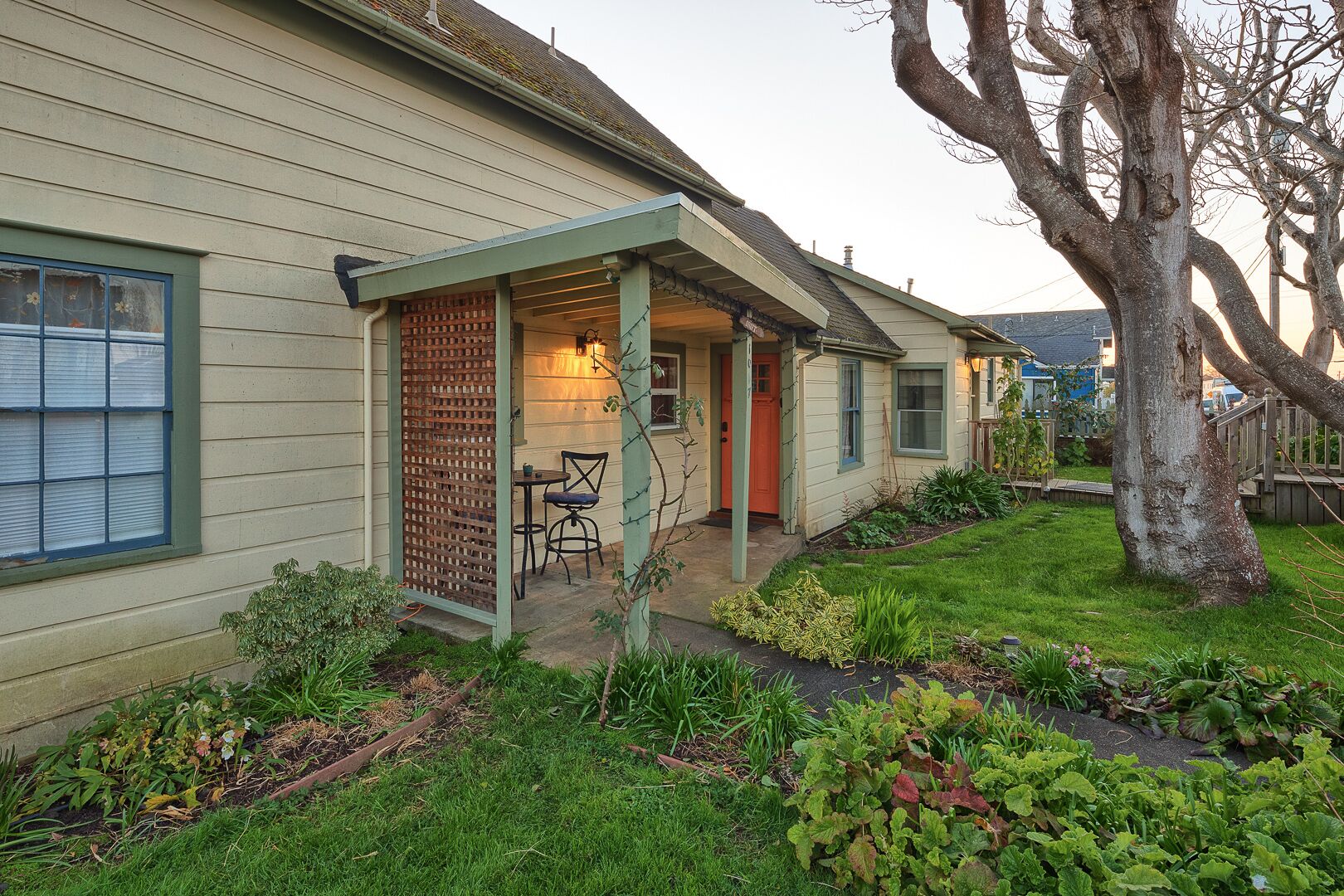 A house with a covered porch, a small table and chair, and a garden with various plants.