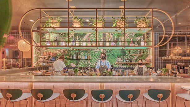 Eine Bar im tropischen Stil, mit einer Theke, Barhocker und einer Flaschenregal.