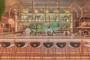 A bar with a tropical theme, featuring a counter, bar stools, and a shelf with bottles.