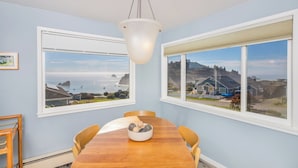 Ein Esszimmer mit Holztisch, zwei Fenstern mit Blick aufs Meer und einer Pendelleuchte.