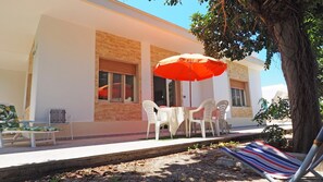 Eine Terrasse mit Tisch, Stühlen, einem roten Sonnenschirm und einem Baum.