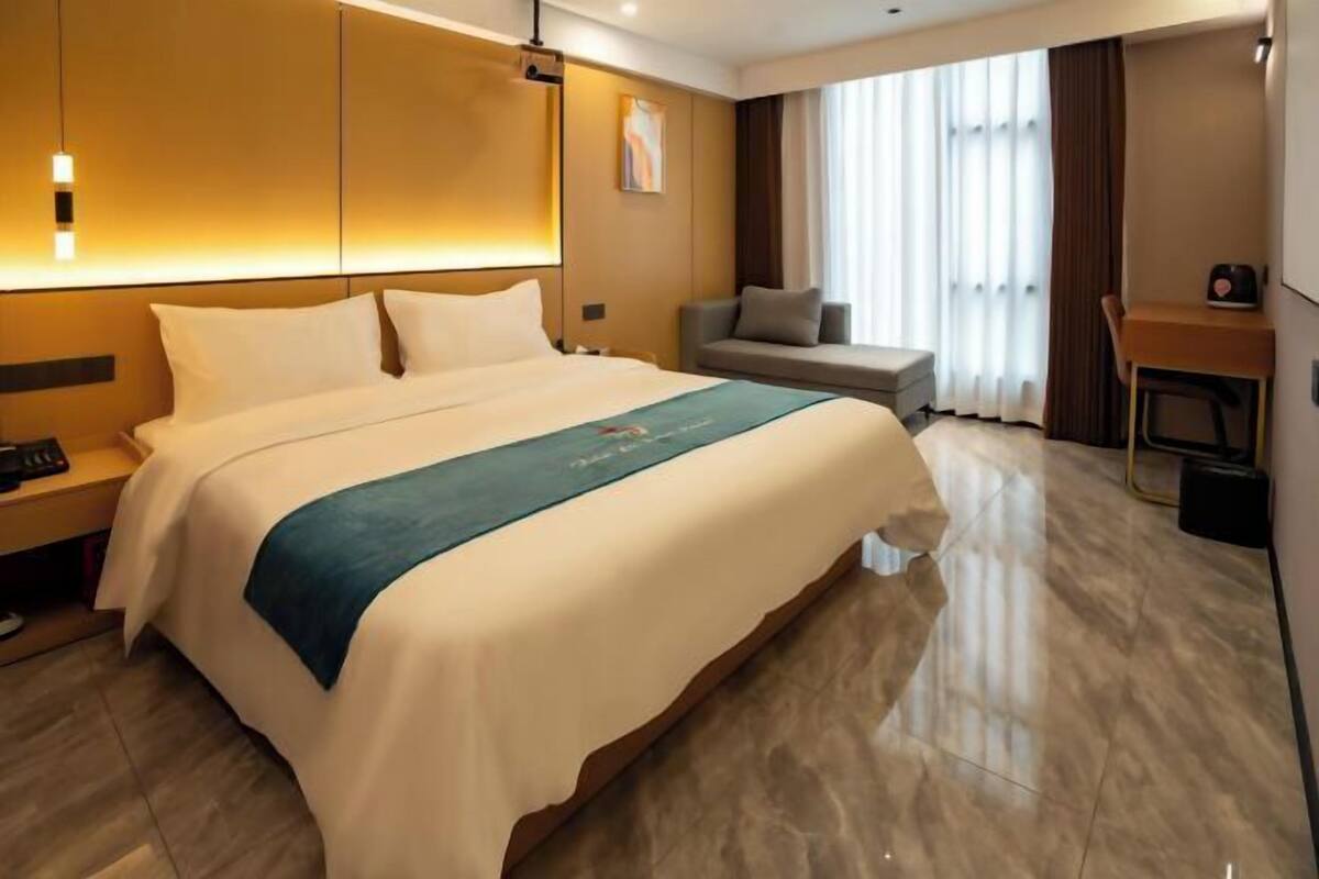 A hotel room with a large bed, bedside tables, a desk, and a window with curtains.