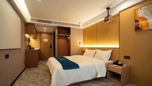 Una habitación de hotel con cama, mesita de noche, armario y proyector.