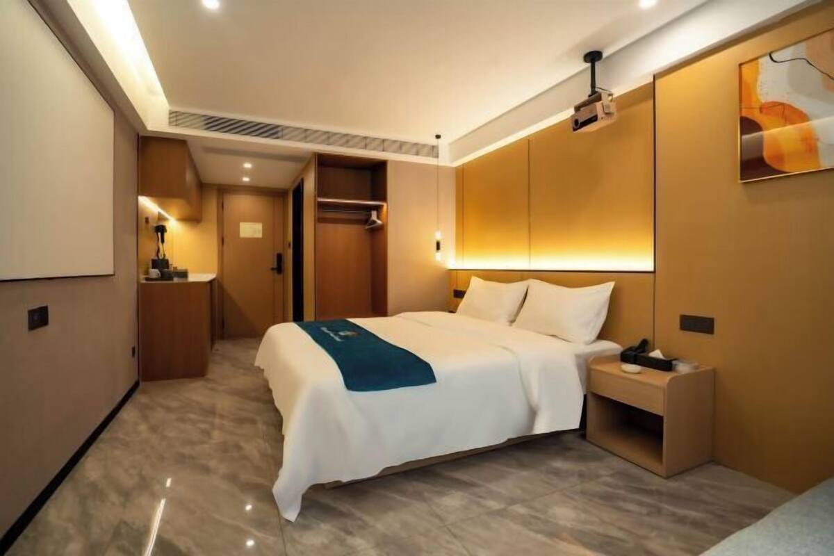 A hotel room with a bed, bedside table, nightstand, wardrobe, and a projector.