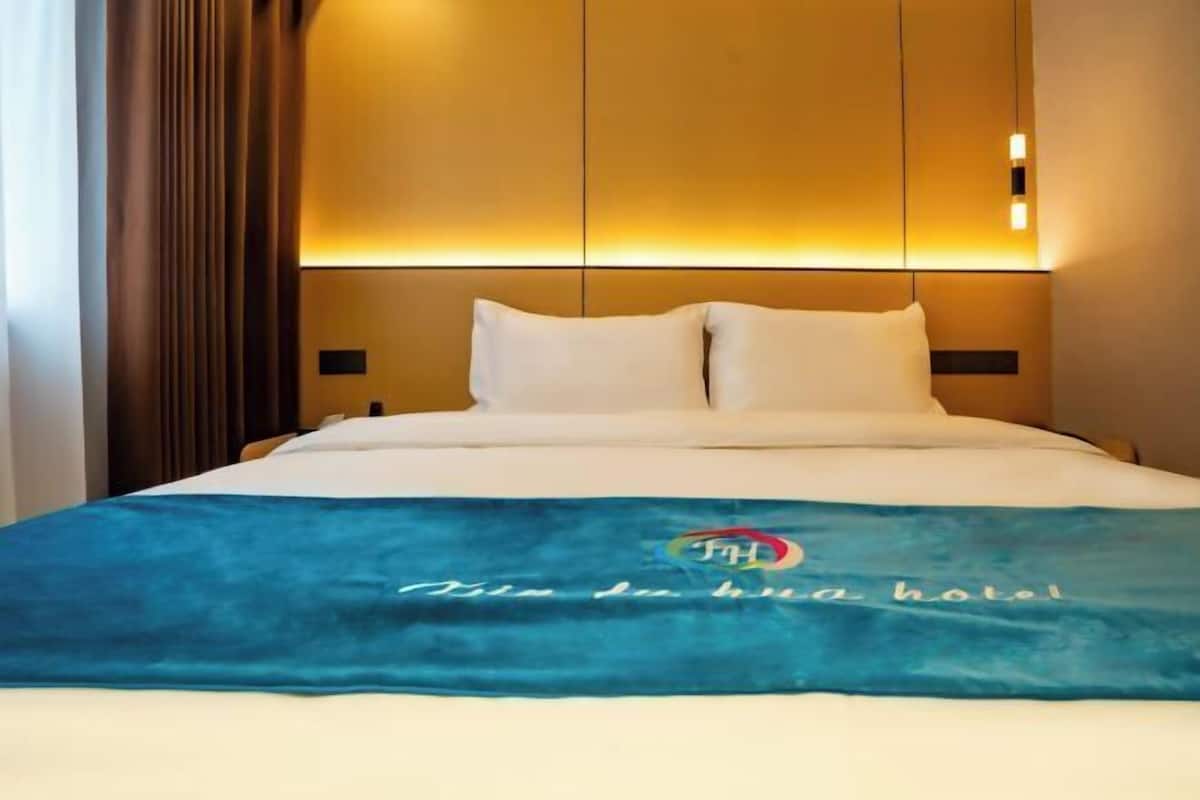 A hotel room with a bed, a blue blanket with text, and a headboard with built-in lighting.