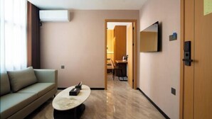Habitación de hotel con sofá, una mesa de centro, televisor montado en la pared y puerta que da a un comedor.