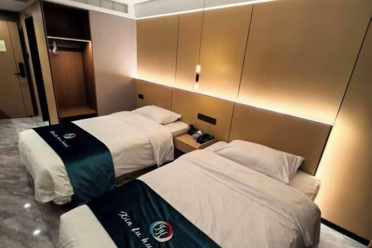 A hotel room with two beds, a wardrobe, and a bedside table.
