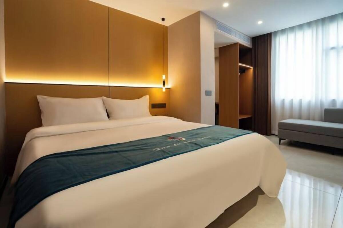 A hotel room with a large bed, a bedside table, a wardrobe, and a seating area with a sofa.