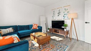 Ein modernes Wohnzimmer mit einem blauen Sofa, einem Holztisch und einem großen Flachbildfernseher.