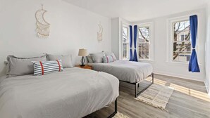 Ein Schlafzimmer mit zwei Betten, einem Nachttisch, einer Lampe und einem Fenster mit blauen Vorhängen.