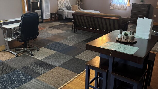 Una habitación con piso de madera, una mesa de comedor con sillas, un sofá, un televisor y un ventilador de techo.