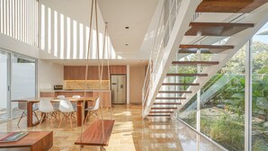 Una cuina moderna amb armaris de fusta, una zona de menjador amb taula i cadires de fusta, i una escala que condueix a una zona exterior amb vegetació.
