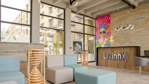A modern lobby with seating areas, a reception desk, and large windows offering views of the building's exterior. - LivinnX Barranquilla 1 (Puerto Colombia)