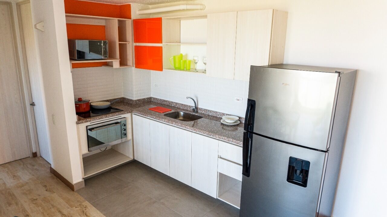 Una cocina compacta con armarios blancos, un refrigerador de acero inoxidable, un microondas y un lavabo.