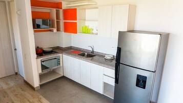 Una cocina compacta con armarios blancos, un refrigerador de acero inoxidable, un microondas y un lavabo.