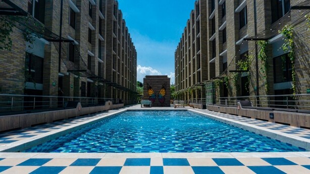 A swimming pool with a checkered pattern, surrounded by brick buildings with vines. - LivinnX Barranquilla 1 (Puerto Colombia)