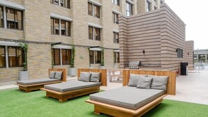 A courtyard with three wooden beds, a brick building, and a modern structure with horizontal lines. - LivinnX Barranquilla 1 (Puerto Colombia)