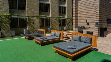A modern outdoor relaxation area with three wooden beds and a bench, surrounded by brick walls and greenery.
