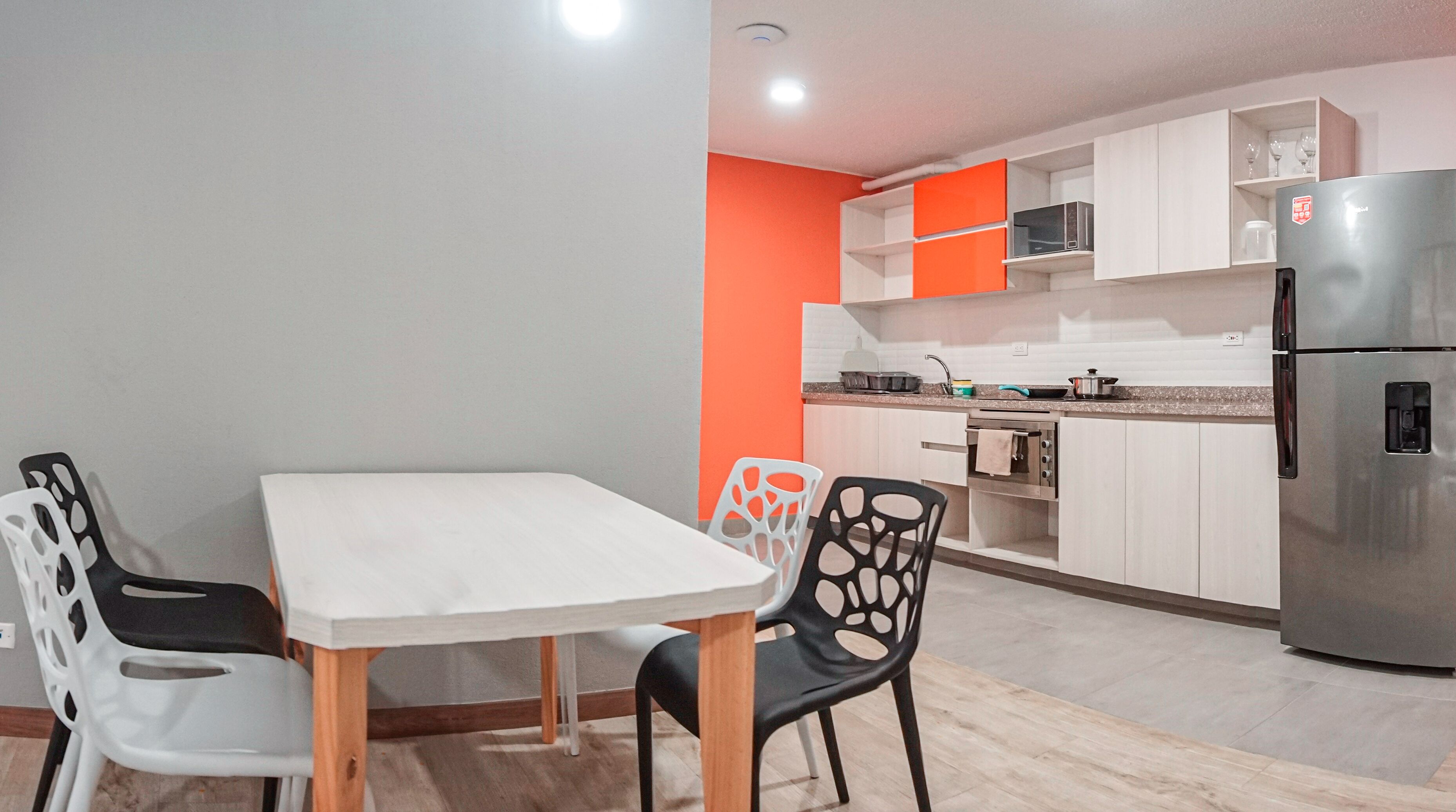 A modern kitchen with white cabinets, a stainless steel refrigerator, and a dining area with a white table and black chairs.